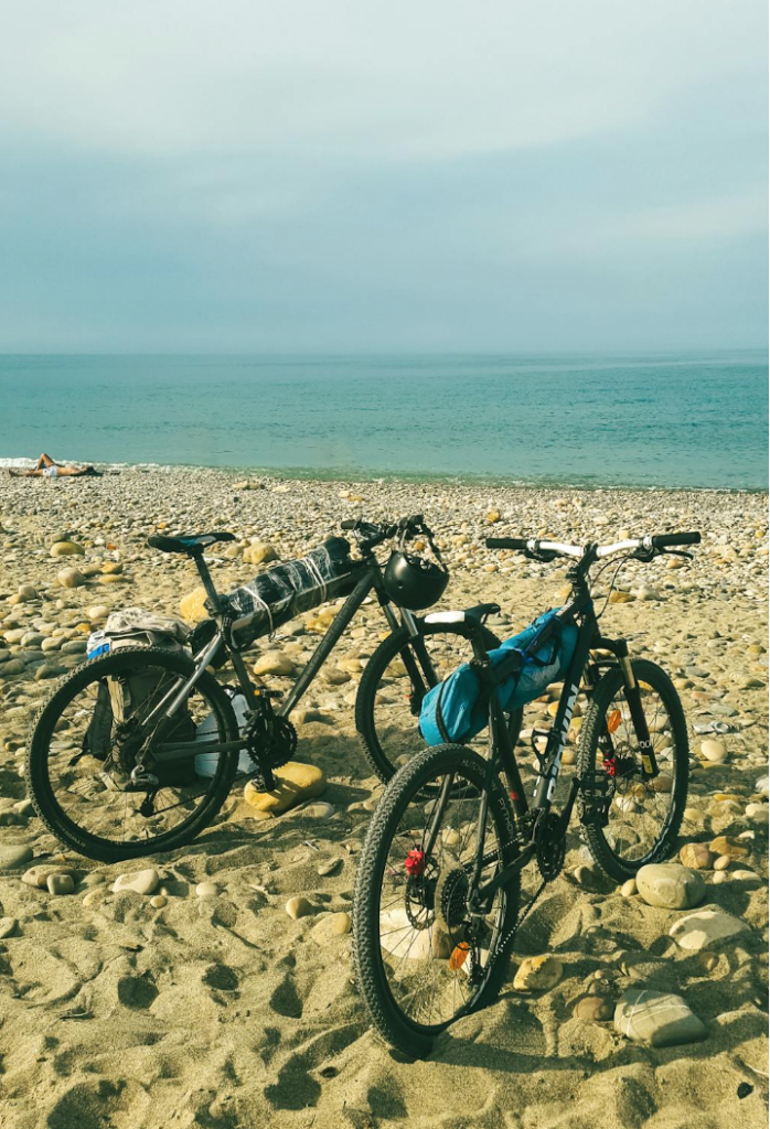 Two bikes packed with gear are stopped in the sand overlooking a beautiful blue ocean view. 